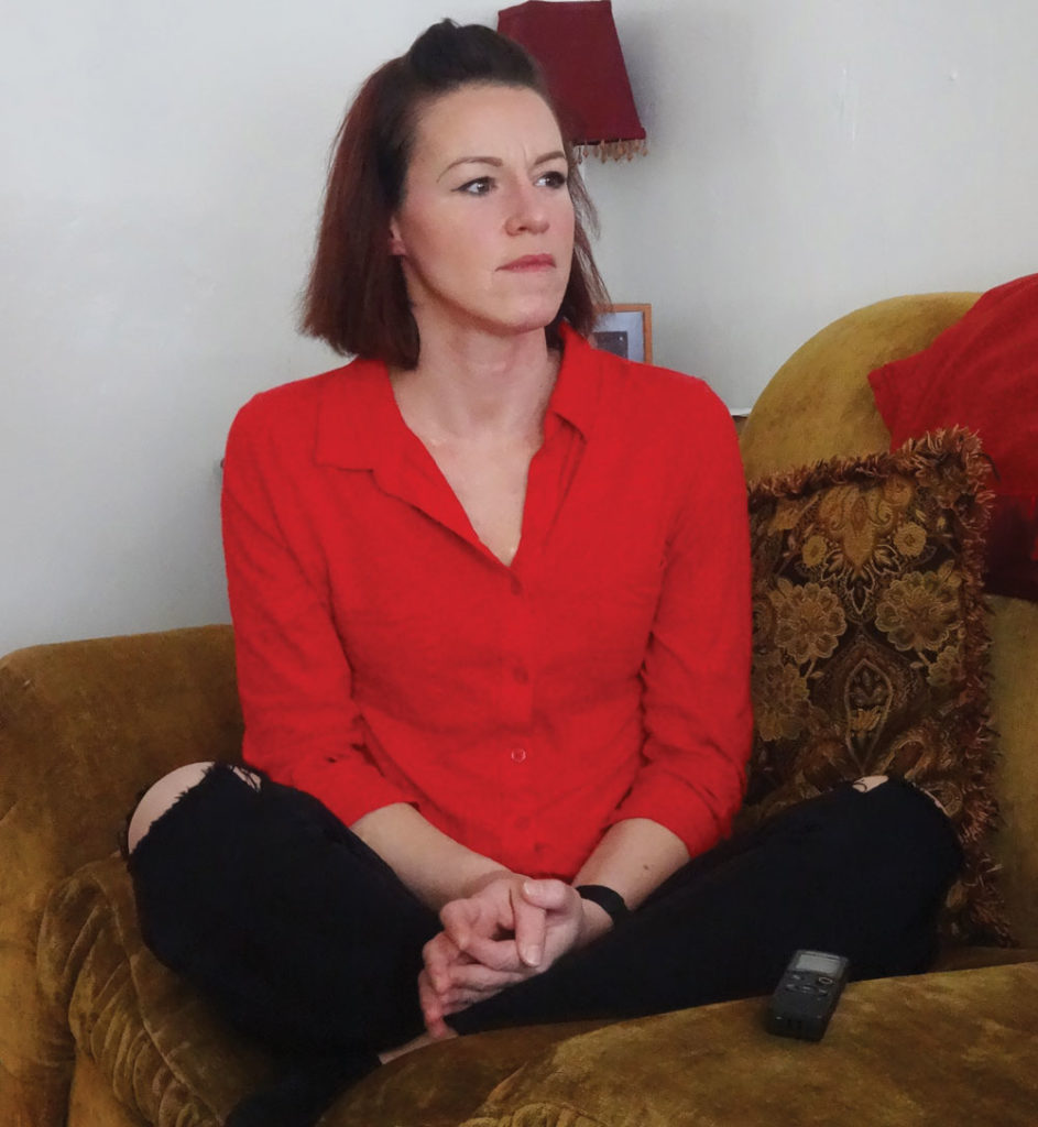 Christine Bemis sits cross legged on a sofa.