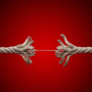 Frayed rope about to break on red background.