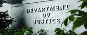 Silver sign of Department of Justice on a classical concrete wall with plants as foreground. Illustration of the concept of enforcement of federal laws